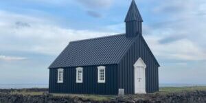 black and white wooden church on green grass field under white clouds and blue sky during